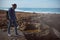 Relaxed young adult backpacked traveler adventurer standing on cliff by Atlantic ocean while waves breaking on the rock