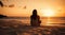 A relaxed young brunette woman or girl wearing a bikini sitting on a deserted tropical beach at sunset or sunrise