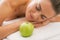 Relaxed young woman with apple laying on massage table