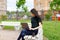 Relaxed young woman in a green T-shirt and with a backpack sitting on a wooden bench, drinking coffee