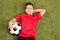 Relaxed youngster lying on pitch and holding a football