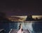 Relaxing in holidays, a man feet on bed at swimming pool at night with city lights and stars on sky background