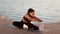 Relaxing pilates . Young flexible african american lady stretching her body, exercising on pier, slow motion, free space