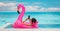 Relaxing woman floating in flamingo inflatable swimming pool toy at luxury resort using mobile phone sunbathing