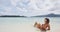 Relaxing woman sunbathing lying in sand on beach in bikini drinking from coconut