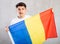 Reliant positive young man holds big national flag of Romania with confident smile showing teeth.