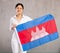 Reliant positive young woman holds big national flag of Cambodia with confident smile showing teeth
