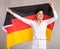 Reliant positive young woman holds big national flag of Germany with confident smile showing teeth.