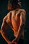 Relief, muscular, athletic male back. Shirtless model with fit body posing against dark studio background