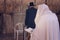 Religious orthodox Jew in the foreground wearing a prayer shawl draped prays at the Western wall, Jerusalem, Israel. Male figure