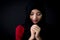 Religious young Muslim woman praying over black background.