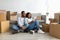Relocation concept. Happy black couple using tablet, searching new furniture while sitting among moving boxes near sofa