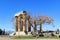 Remaining columns of Temple of Apollo at ancient Corinth Greece with tree in foreground and snow capped mountians in the distance