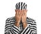 Remorseful prisoner in striped uniform with handcuffs hiding his face on white background