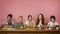 Remote schooling. Group of boys and girls with learning materials and devices sitting at desk over pink background