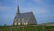 Remote view of unrecognizable tourists walking around small old church in Etretat found on top of cliff fronting sea, on