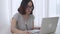 Remote working at home office at afternoon, concentrate Asian woman working desk near window in living room, typing computer lapto