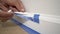 Removing masking tape from molding. A painter pulls of blue painter`s tape from the wall to reveal a clean edge baseboard