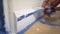 Removing masking tape from moulding. A painter pulls of blue painter`s tape from the wall to reveal a clean edge baseboard