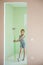 Renovation concept of beautiful thin little girl stand with paint roller in new green beige flat apartment