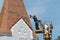 Repair and reconstruction of the old roof made of red tiles of a century-old building. The worker is in the basket of a crane and