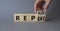 Repair and Repeat symbol. Hand turns cubes and changes the word Repeat to Repair. Beautiful grey background. Businessman hand.