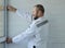 A repair worker, a measurer, a furniture maker dressed in a white jumpsuit measures the height of the wall at the window to obtain