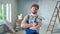 Repairman in blue overalls is looking confidently at camera and crossing arms with paint roller. Portrait of redhead man