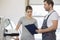 Repairman holding clipboard while conversing with female customer in repair shop