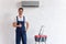 Repairman showing thumb up while standing under air conditioner near stepladder and toolbox