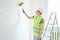 Repairs in the apartment, a man in a green vest and a white helmet stands in a white room with a roller in his hands