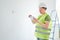 Repairs in the apartment, a man in a green vest and a white helmet is in a white room with a tablet in his hands