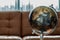 Replica globe on brown leather sofa and white curtains on background