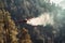 Rescue firefighting aircraft extinguishes forest fire by dumping water on burning pine forest. Front view of airplane on