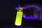 Researcher hand checking yellow close up photochemical reaction in glass vial under UV light in a dark chemistry laboratory