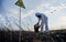 Researcher in protective suit collecting plastic garbage into black waste bag outdoors on a sunny day