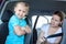 Resentful child ignoring mother forcing to seat into infant safety seat