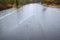 Residential street with water flooding woodland and roadway, still raining, abandoned car in distance