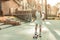 Resolute young lady in white dress riding on a skateboard