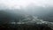 Resort at foot of mountains in cloudy weather. Scenic top view of mountain landscape with snowy peaks in fog and small