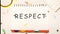 respect word on a checkered notebook on a light table next to a magnifying glass, paper clips, stationery buttons, a calculator