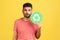Responsible self confident man with beard in striped t-shirt holding green recycling sign in hand and seriously looking at camera