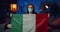 Responsible young man in protective mask holding italian flag while sitting on sofa. Millennial guy staying at home due