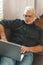 Rest with a laptop at home. A gray-haired bearded man lies with a computer on the couch. He looks intently