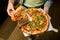 Restaraunt manager hold in hands wooden tray with fresh delicious pizza and separates one slice