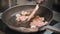 Restaurant cooking - chef roasts bacon pieces in a frying pan