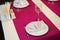 Restaurant table setout with white plates, silverware and magenta decoration