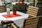 Restaurant tables and wooden chairs in a covered terrace area outdoors. Tables are covered with white tablecloth