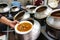 A restaurant worker spooning a mutton curry from the big pot