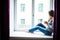 Resting and thinking woman. Calm girl with cup of tea or coffee sitting and drinking on the window-sill at home.